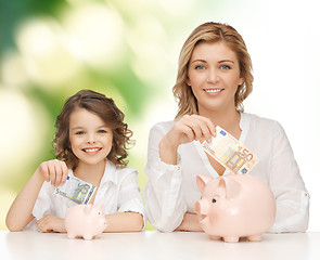 Image showing mother and daughter putting money to piggy banks