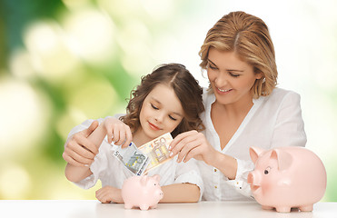 Image showing mother and daughter putting money to piggy banks