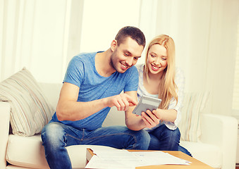 Image showing smiling couple with papers and calculator at home