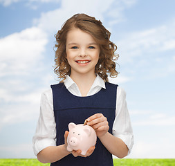 Image showing smiling girl putting coin into piggy bank