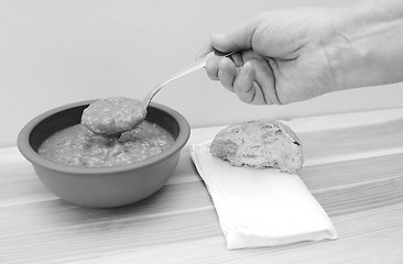 Image showing Hand holds spoonful of soup with bread roll and napkin on table