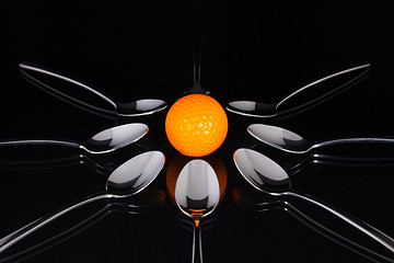 Image showing Teaspoons and orange golf ball on the black glass table 