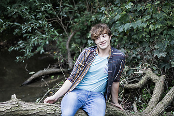 Image showing young man sitting on branch over a stream