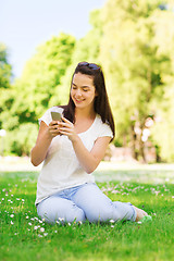 Image showing smiling young girl with smartphone sitting in park