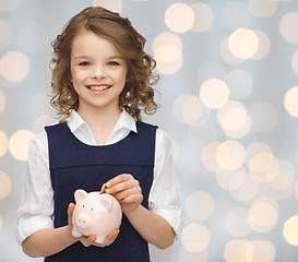 Image showing smiling girl putting coin into piggy bank