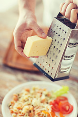 Image showing close up of male hands grating cheese over pasta