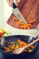 Image showing close up of male hand adding peppers to wok