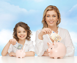 Image showing mother and daughter putting money to piggy banks