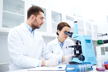Image showing scientists with clipboard and microscope in lab