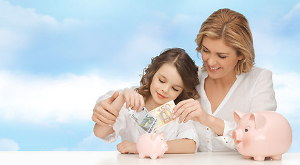 Image showing mother and daughter putting money to piggy banks