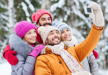 Image showing smiling friends with camera in winter forest