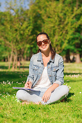 Image showing smiling young girl with notebook writing in park