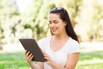 Image showing smiling young girl with tablet pc sitting on grass