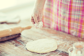 Image showing closeup of female hand sprinkling dough with flour