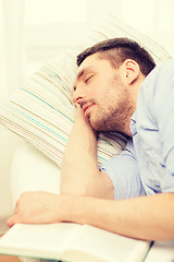 Image showing calm young man lying on sofa at home with book