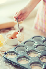 Image showing close up of hand filling muffins molds with dough