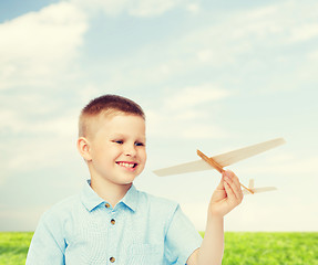 Image showing smiling little boy holding a wooden airplane model