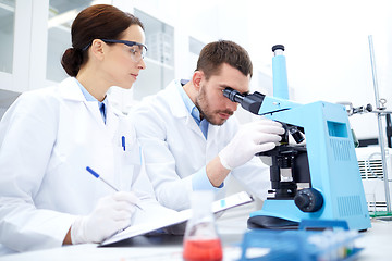 Image showing scientists with clipboard and microscope in lab