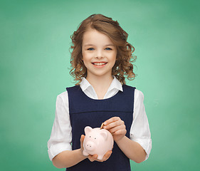 Image showing smiling girl putting coin into piggy bank