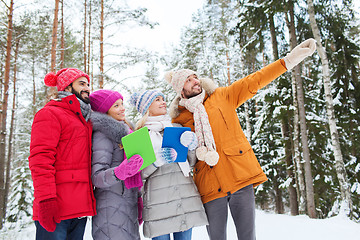 Image showing smiling friends with tablet pc in winter forest