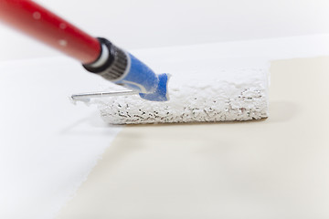 Image showing Paint roller with white paint on wall