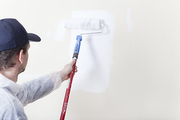 Image showing Painter paints wall with paint roller white