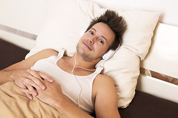 Image showing Smart guy lies in bed and listens to music