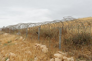 Image showing Barbed tape or razor wire fence across the desert hill on cloudy day