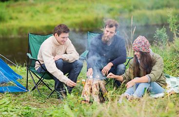 Image showing smiling tourists cooking marshmallow in camping