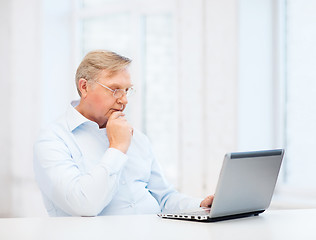 Image showing old man in eyeglasses working with laptop at home