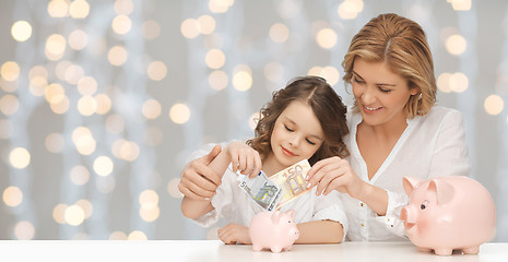 Image showing mother and daughter putting money to piggy banks