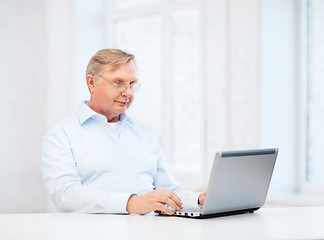 Image showing old man in eyeglasses working with laptop at home