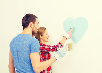 Image showing smiling couple painting small heart on wall