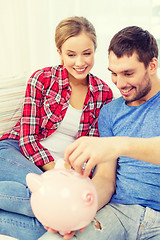 Image showing smiling couple with piggybank sitting on sofa