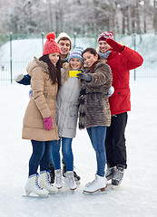 Image showing happy friends with smartphone on ice skating rink