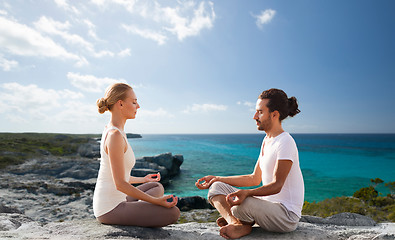 Image showing happy couple meditating in lotus pose on beach