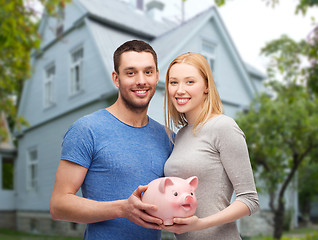 Image showing smiling couple holding piggy bank over house