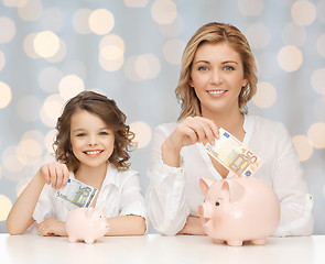 Image showing mother and daughter putting money to piggy banks
