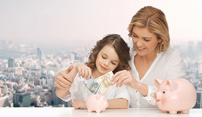 Image showing mother and daughter putting money to piggy banks