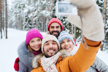 Image showing smiling friends with camera in winter forest