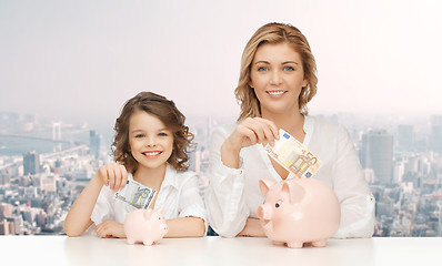 Image showing mother and daughter putting money to piggy banks