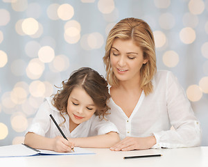 Image showing happy mother and daughter writing in notebook