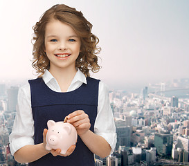 Image showing smiling girl putting coin into piggy bank