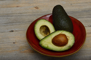 Image showing whole avocado and two halves on a red ceramic saucer