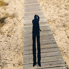 Image showing Elongated Shadow Jumping Man on a Wooden Walkway