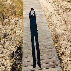 Image showing Elongated Shadow Jumping Man on a Wooden Walkway