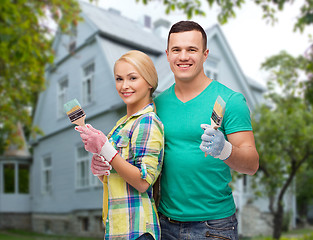 Image showing smiling couple with paint brushes over house