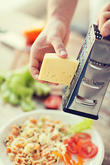 Image showing close up of male hands grating cheese over pasta