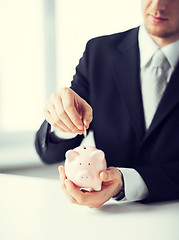 Image showing man putting coin into small piggy bank