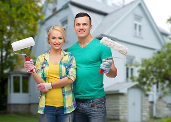 Image showing smiling couple with paint rollers over house